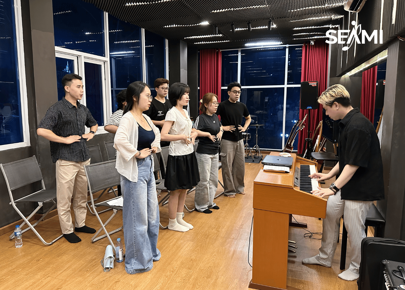 Giáo viên SEAMI đệm đàn, lớp tập thể đứng warm-up hơi thở
